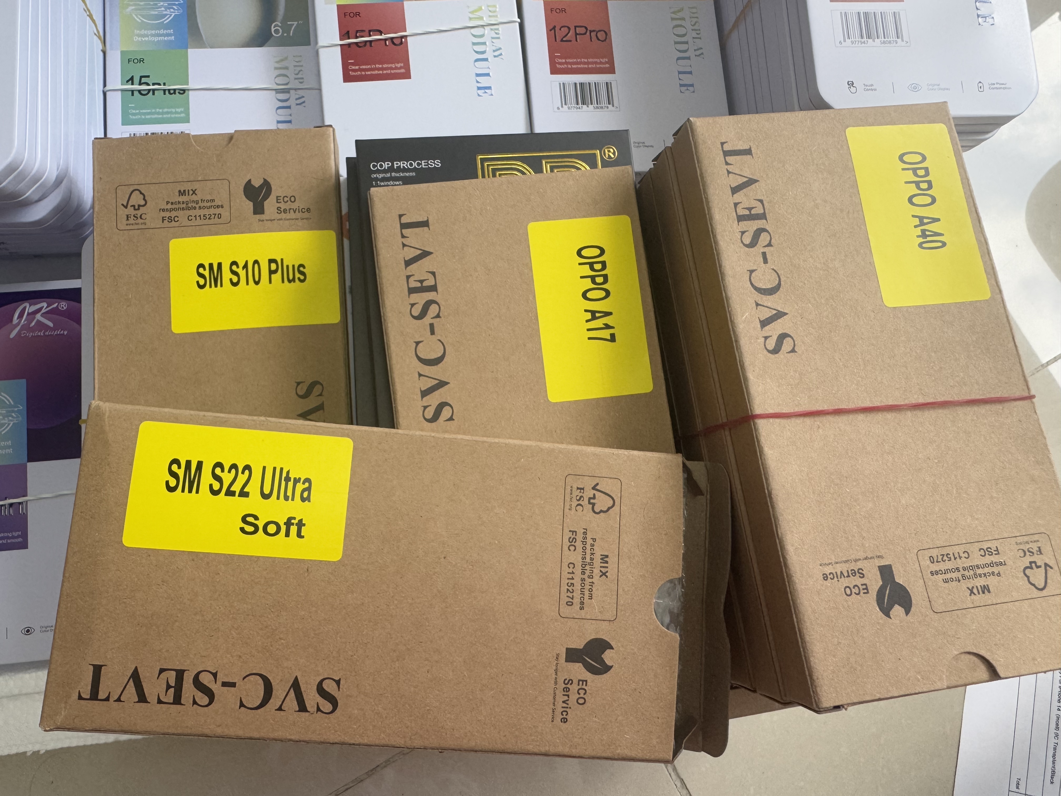 Wholesale phone screen packaging boxes from SVC-SEVT brand stacked with bubble wrap showing inventory for Samsung S10 Plus, OPPO A17, OPPO A40 and Samsung S22 Ultra.
