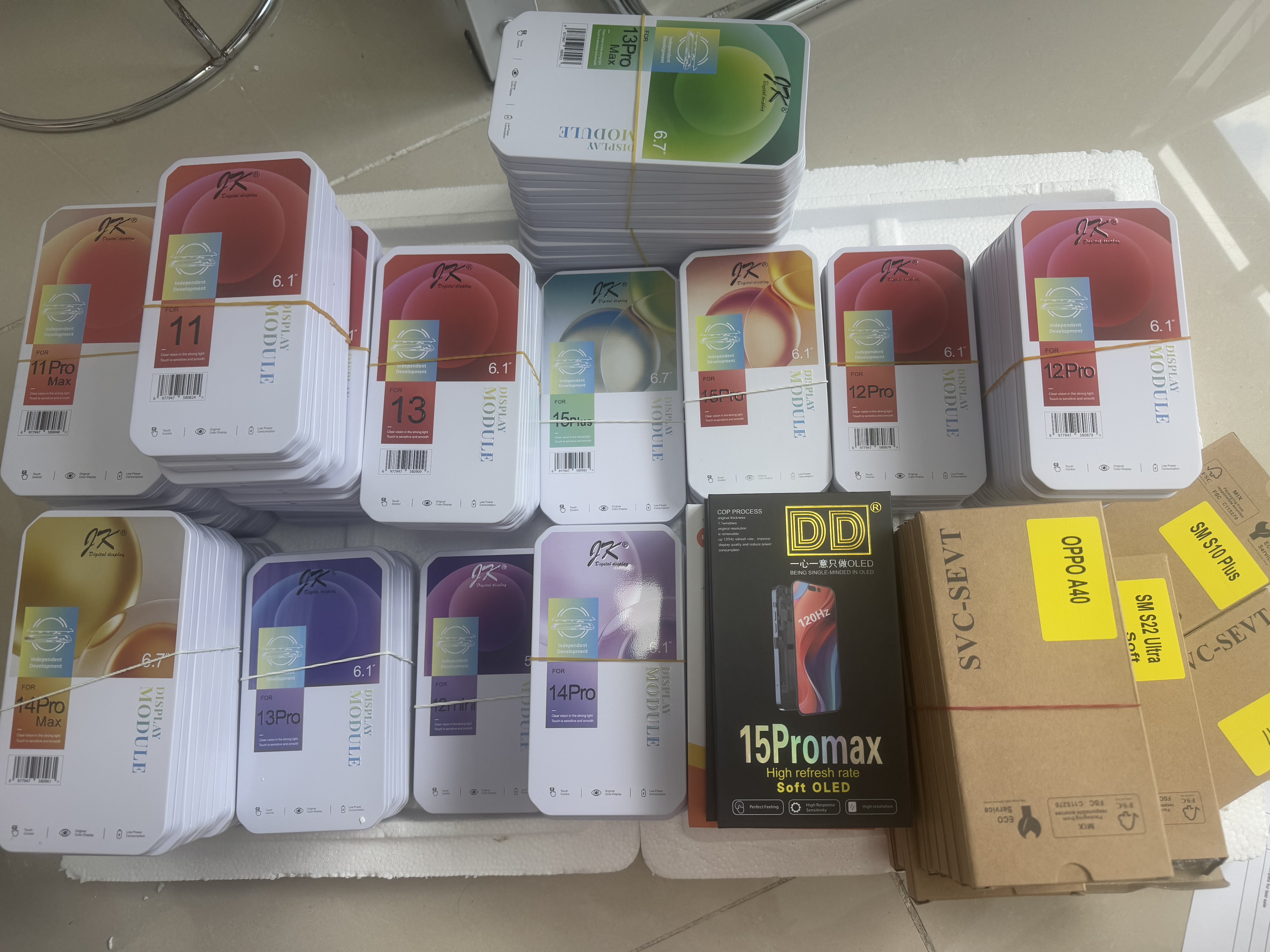 Warehouse inventory stack of phone screen replacement parts including JK, DD and SVC-SEVT brand boxes for various iPhone and Samsung models.