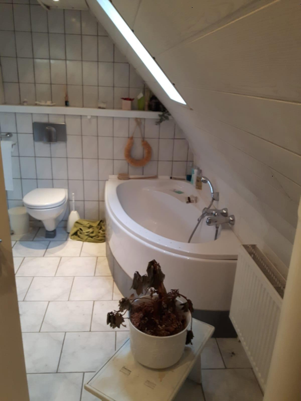 Gammelt badeværelse før renovering – hvide småfliser og hjørnekar